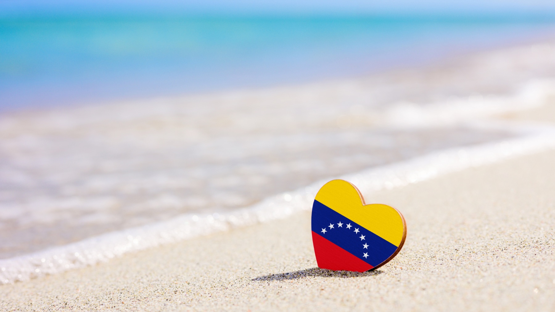 A heart painted with the Venezuelan flag resting on a sandy beach